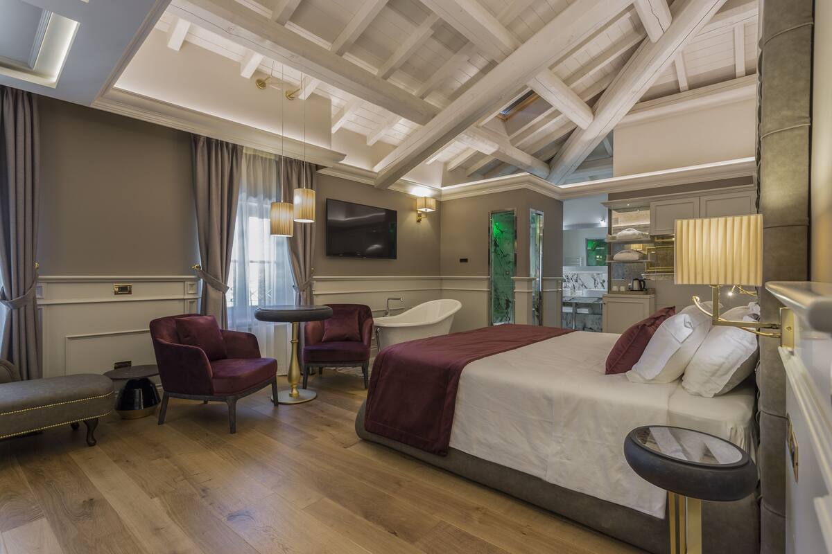 A hotel room with a bed, a desk, a chair, a vanity, and a bathtub.