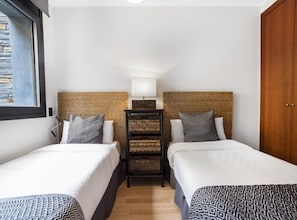 Two single beds with woven headboards and a nightstand with a lamp and baskets.