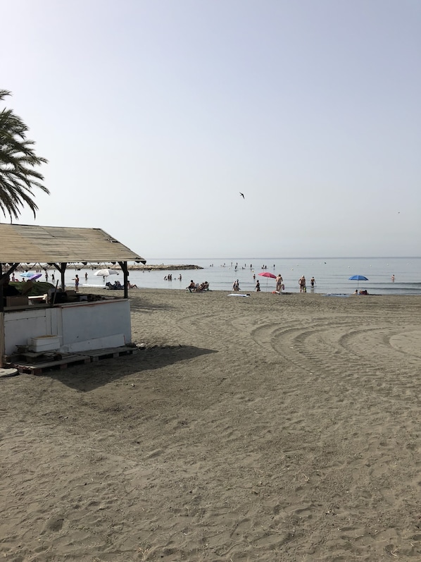 Une plage avec une structure en bois, peut-être un kiosque ou une petite boutique, et une vue dégagée sur la mer.