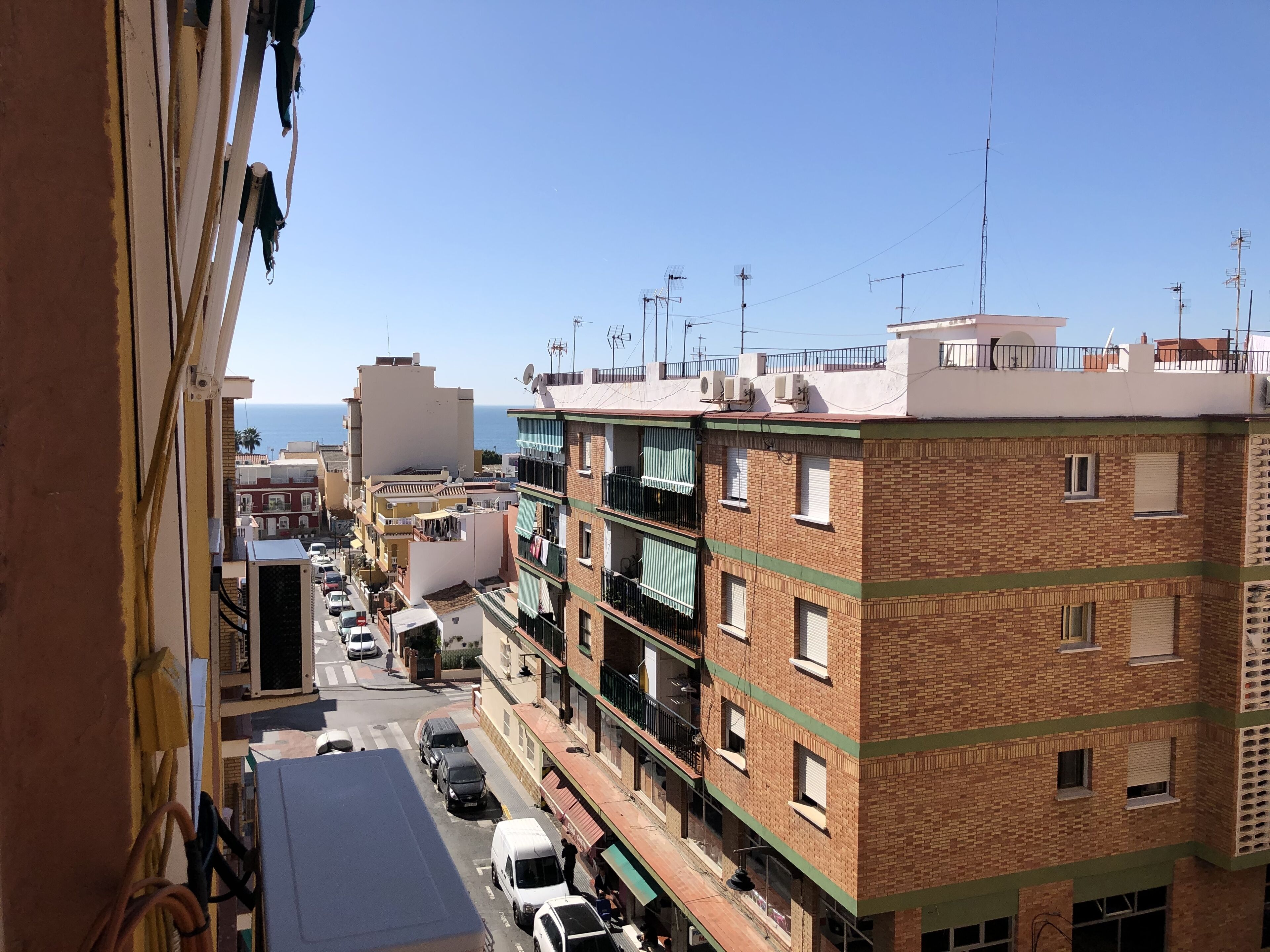 A multi-story building with balconies, a street view, and a clear sky.