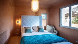 A bedroom with a large bed, a headboard, a bedside table, a chair, a window, and a wall-mounted light fixture. - Villa Luxi private pool, jacuzzi, housekeeping and concierge (Is Molas)