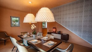 A dining area with a wooden table set for four, surrounded by chairs, with patterned wallpaper and a decorative vase on the sideboard. - Villa Luxi private pool, jacuzzi, housekeeping and concierge (Is Molas)