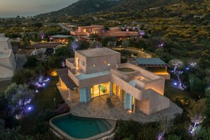 A modern, multi-story villa with a pool, surrounded by landscaped gardens and a mountainous backdrop. - Villa Luxi private pool, jacuzzi, housekeeping and concierge (Is Molas)