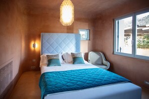A bedroom with a large bed, a headboard, a bedside table, a chair, a window, and a wall-mounted light fixture. - Villa Luxi private pool, jacuzzi, housekeeping and concierge (Is Molas)
