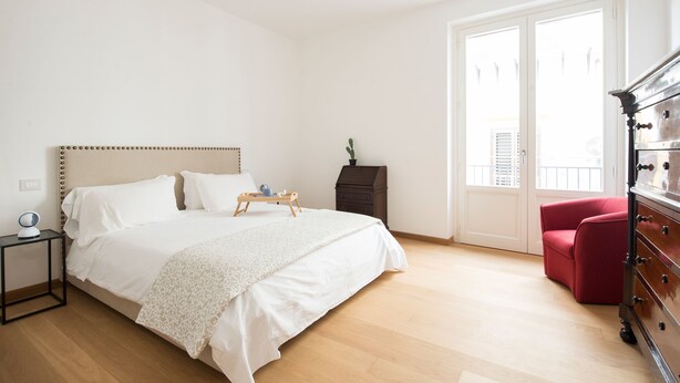 Een slaapkamer met een bed, nachtkastje, kaptafel en een rode stoel.
