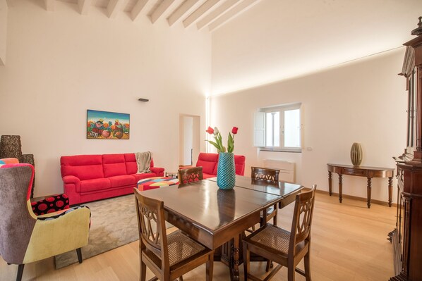 A spacious living room with a red sofa, a wooden dining table, and a colorful rug.