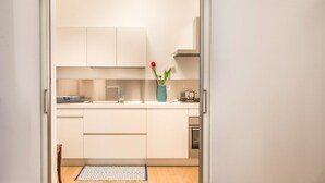 Een kleine keuken met witte kastjes, een spoelbak en een vaas met bloemen.