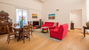 Een ruime woonkamer met een houten eettafel, een rode bank en kleurrijke kunstwerken aan de muren.