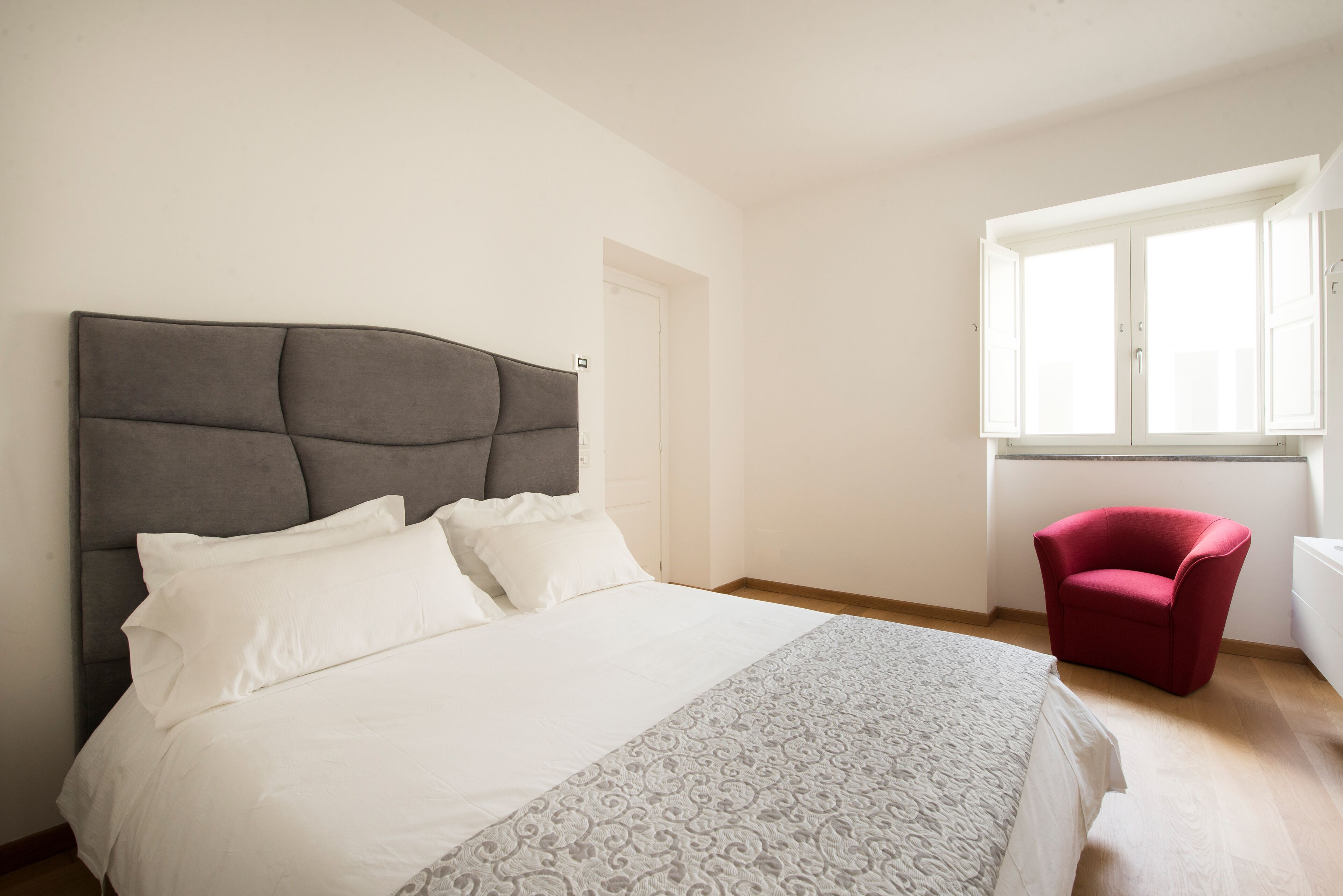 Una camera da letto con un letto grande, una poltrona rossa e una finestra con persiane bianche.