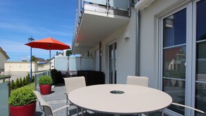 A balcony with a round table and chairs, a red umbrella, and potted plants. - Haus Sonne (Mönchgut-Granitz)