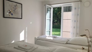 A bedroom with two beds, a window with curtains, a bedside lamp, and a framed artwork on the wall. - Haus Sonne (Mönchgut-Granitz)