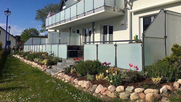 A two-story building with a balcony, a name sign 'Sonne', and a garden with flowers and rocks. - Haus Sonne (Mönchgut-Granitz)