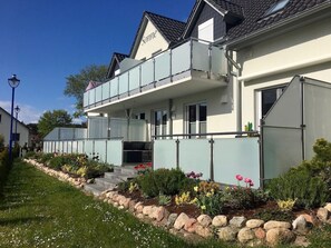 Ein zweistöckiges Gebäude mit Balkon, einem Schild mit der Aufschrift 'Sonne' und einem Garten mit Blumen und Steinen.