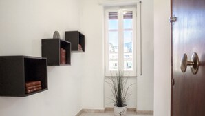 Ein Flur mit Holztür, einem Fenster mit Jalousien und einem Blumentopf.