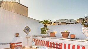 A rooftop terrace with a wooden table and chairs, potted plants, and a view of the cityscape. - Terrazza al Capo by Wonderful Italy (Palermo)
