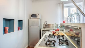 A compact kitchen with a refrigerator, microwave, gas stove, and a window with curtains. - Terrazza al Capo by Wonderful Italy (Palermo)