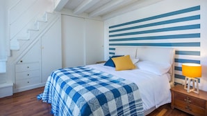 A bedroom with a checkered bedspread, a nightstand with a lamp, a wooden dresser, and a staircase. - Terrazza al Capo by Wonderful Italy (Palermo)