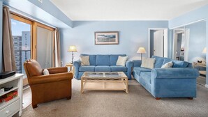 Una sala de estar con un sofá azul, un sillón de cuero marrón y una mesa de centro de vidrio.
