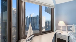 Una habitación de hotel moderna con ventanas amplias, un modelo de velero, una lámpara de noche y una cama bien hecha.