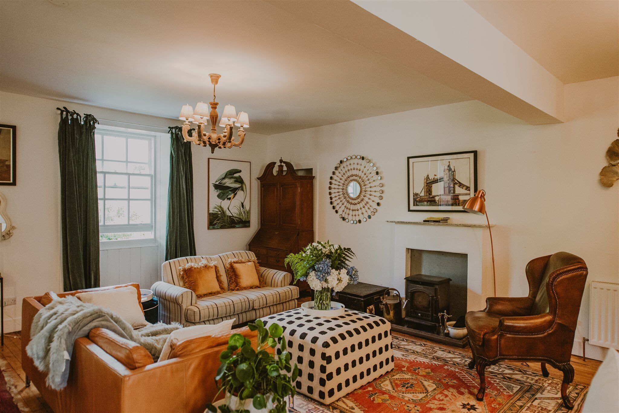 A cozy living room with a fireplace, striped sofa, and a patterned ottoman.