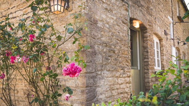 A stone building with a door and windows, surrounded by greenery and flowers.