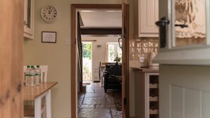 A hallway leading to a living area with a stone floor, a clock on the wall, and a door leading to another room.