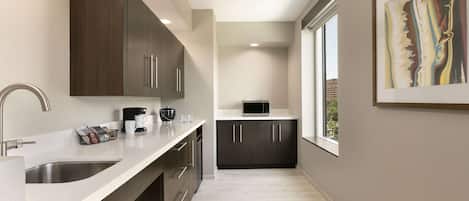 A modern kitchen with dark cabinets, a white countertop, and a window providing a view of the outside.