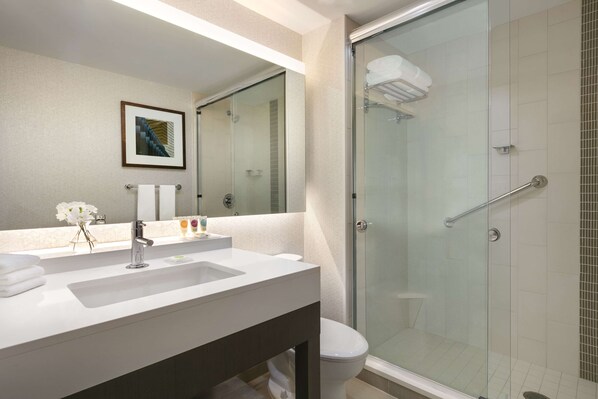 A modern bathroom with a glass shower enclosure, a white sink, and a framed picture on the wall.