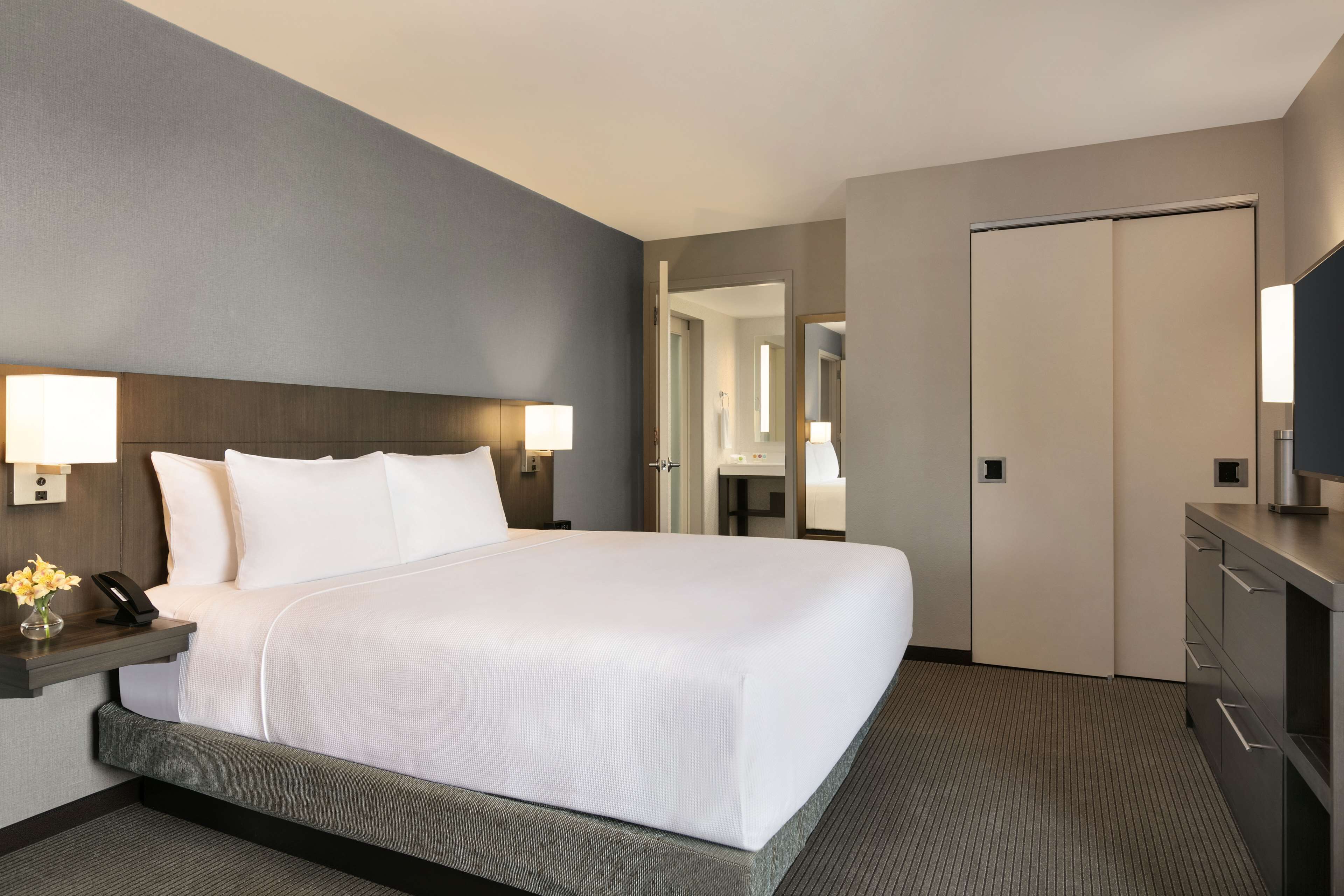 A hotel room with a large bed, bedside lamps, a desk with a phone, and a mirror.