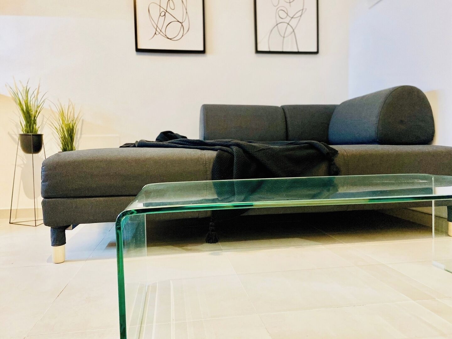 A modern living room with a grey sofa, a glass coffee table, and two abstract art pieces on the wall.