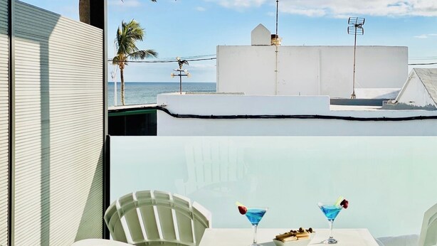 Una terraza con sillas blancas y una mesa, dos cócteles azules y un tazón de nueces.