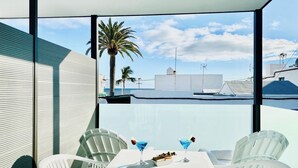 Un espacio moderno para comer al aire libre con sillas blancas y una mesa, con vistas a un puerto deportivo con barcos y palmeras.