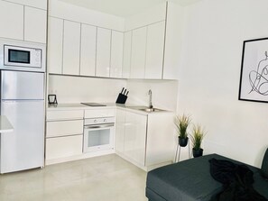 A modern kitchen with white cabinetry, a built-in microwave, a sink, and a small countertop. There is a black knife block on the counter and two potted plants near the sink. - Canaryislandshost l Brisa del Atlántico (Playa Honda)