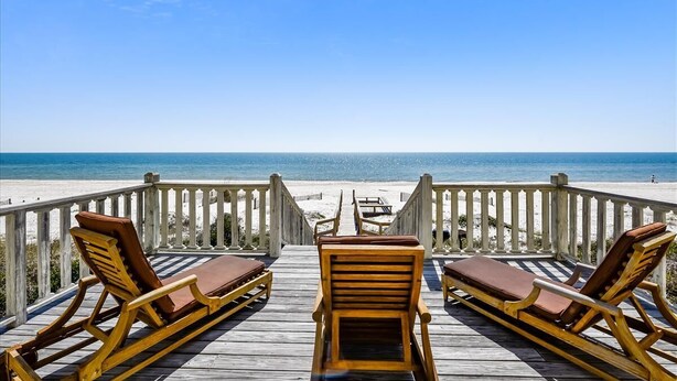 Une terrasse en bois avec des chaises longues donnant sur une plage.