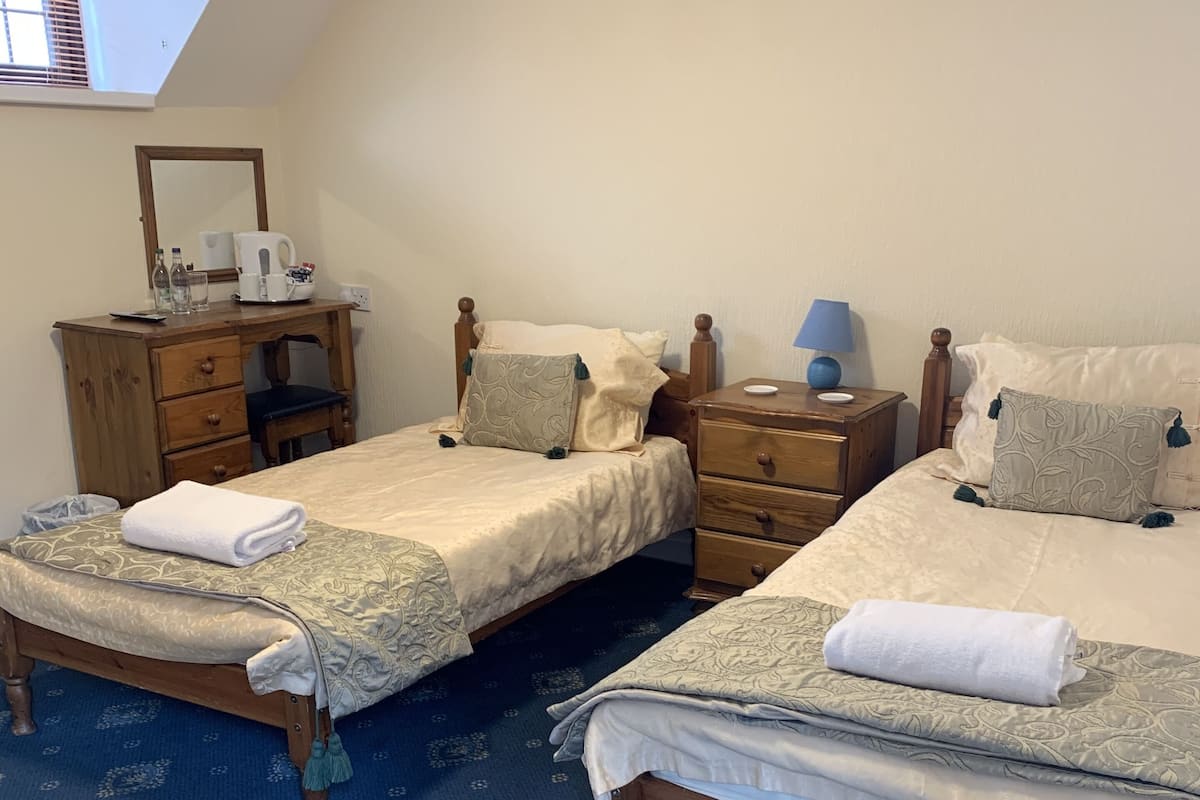 Une chambre avec deux lits, une commode en bois, un bureau et un miroir.