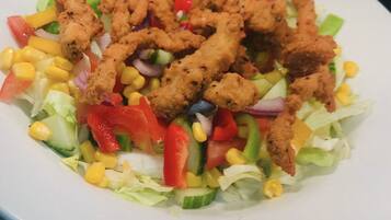 Ensalada con maíz, lechuga y pimientos rojos, coronada con trozos de pollo frito.