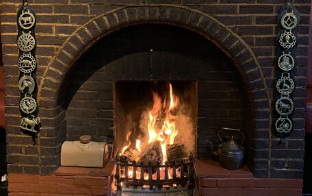 A brick fireplace with a fire, flanked by decorative metal brackets and a framed picture above.