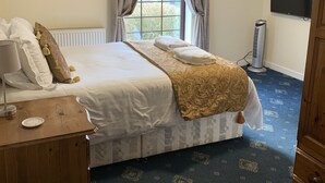 Ein Schlafzimmer mit einem großen Bett, einem Nachttisch, einem an der Wand montierten Fernseher und einem Fenster mit Vorhängen.