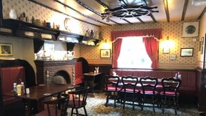 Ein traditionelles Pub mit Kamin aus Backstein, Holzmöbeln und einem gemusterten Teppich.
