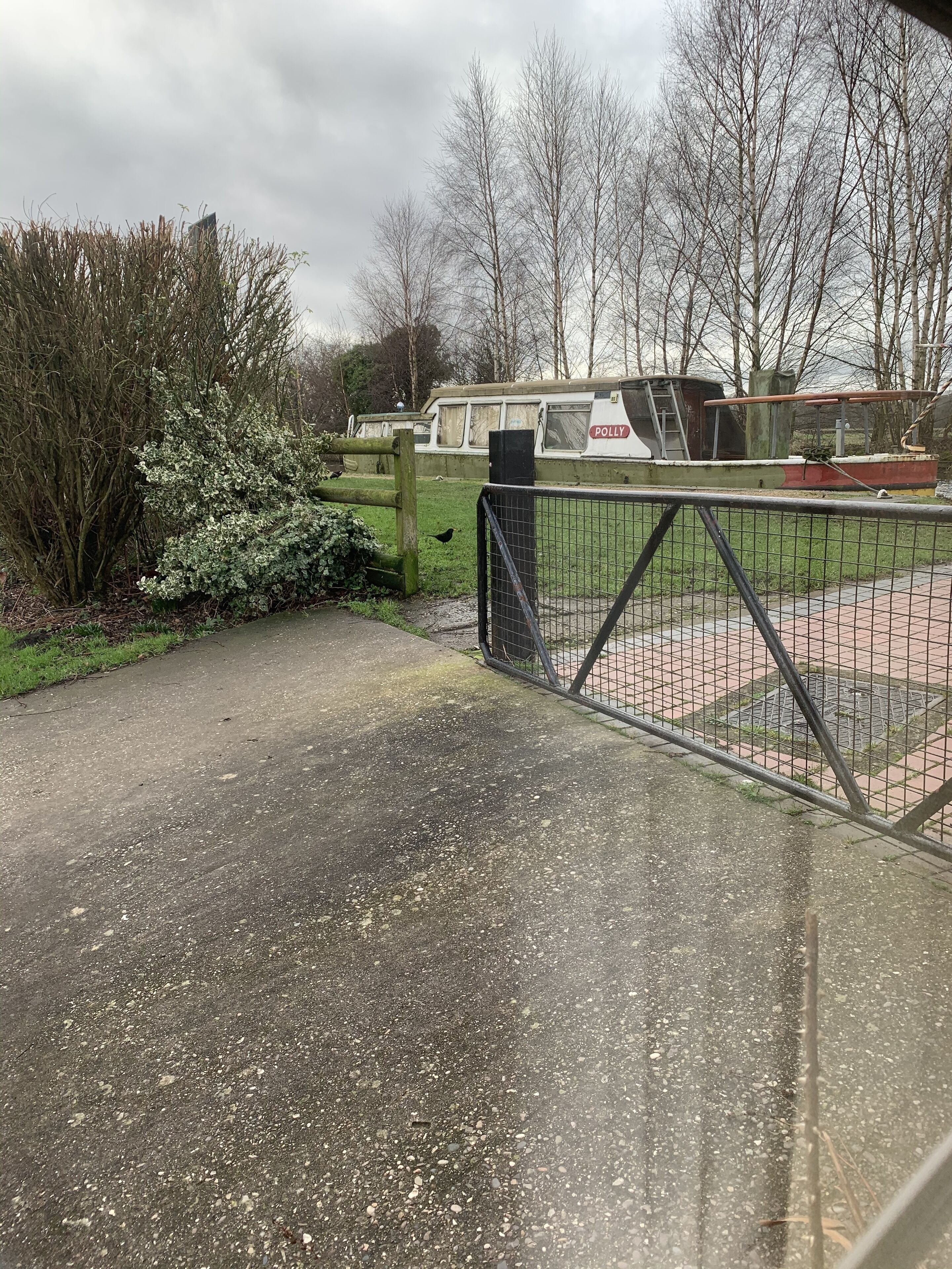 A paved pathway leading to a fenced area with a boat named "POLLY" in the background.