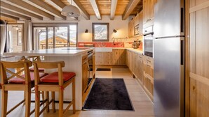 Een moderne keuken met houten kastjes, een roestvrijstalen koelkast en een eethoek met houten stoelen en een zwart vloerkleed.
