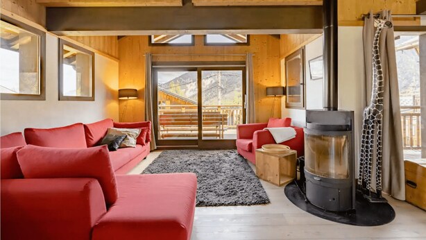 Een gezellige woonkamer met rode banken, een open haard en uitzicht op een houten terras.