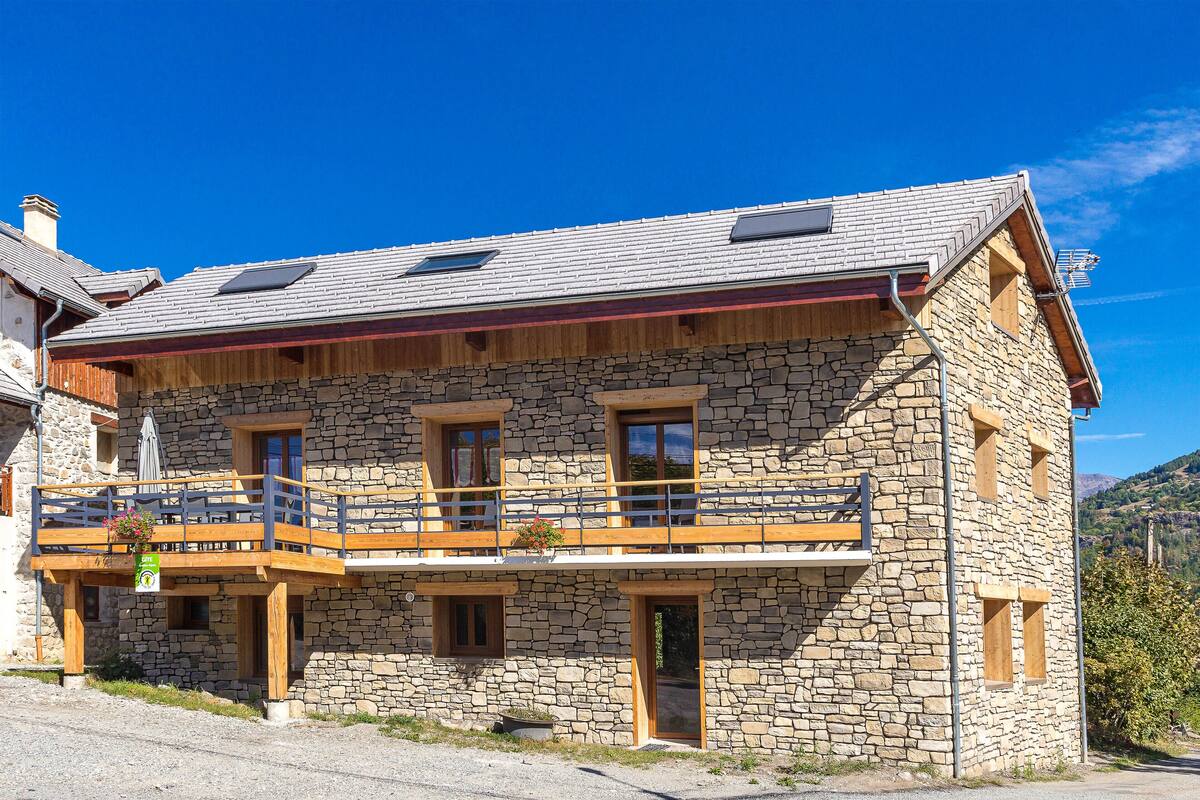 Un edificio de piedra con balcón, varias ventanas y una terraza de madera.