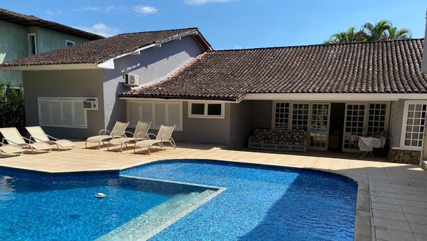 En swimmingpool med krystalklart, blåt vand, omgivet af liggestole og en overdækket terrasse.