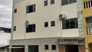 A two-story building with a sign for 'Hotel Pousada do Sol' indicating it is a hotel. There are multiple windows on the facade, and a car is parked in front.