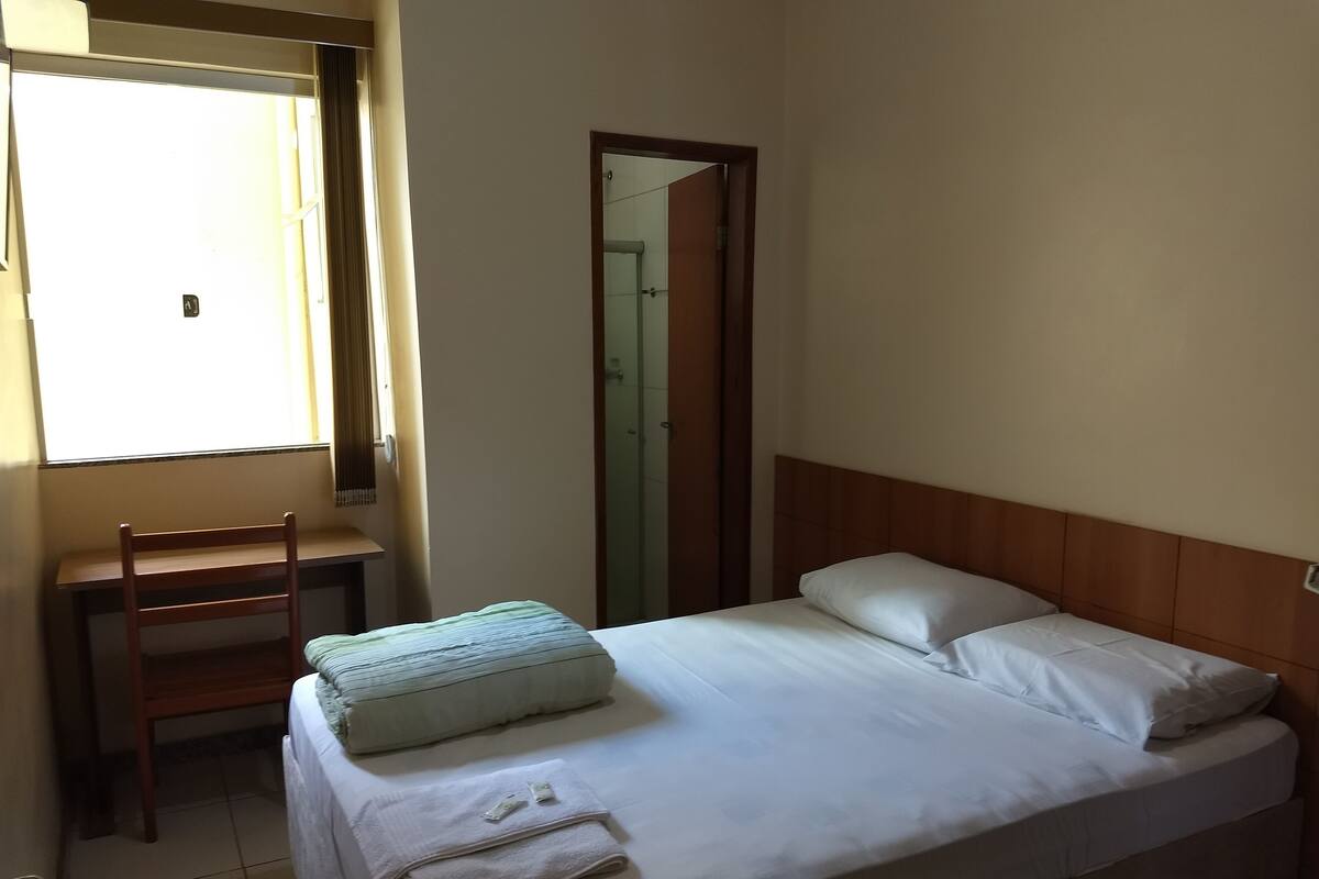 A simple, clean room with a bed, a chair, and a window.