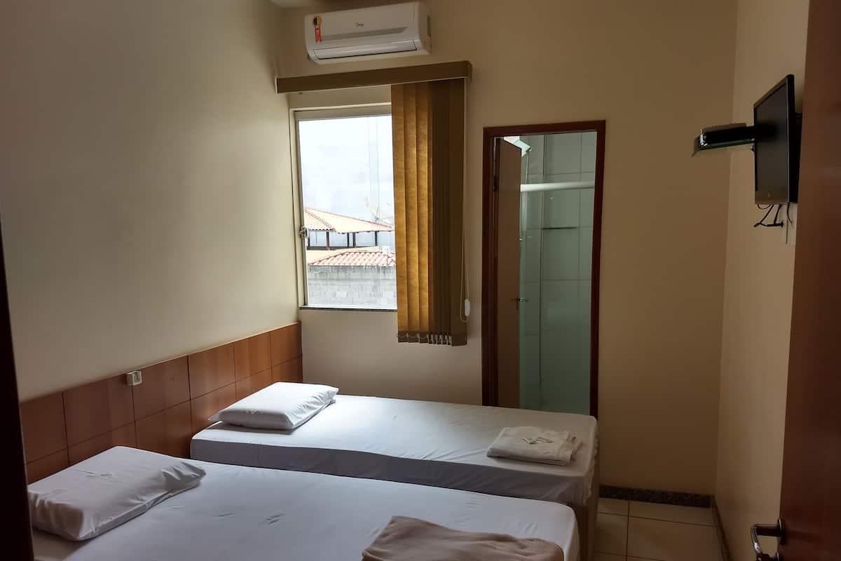 A hotel room with two beds, a window with curtains, a TV mounted on the wall, and a door leading to a bathroom.