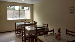 A dining area with wooden chairs and tables, a window with a view of a street, and a 'No Smoking' sign on the wall. - Hotel Pousada do Sol (Uba)