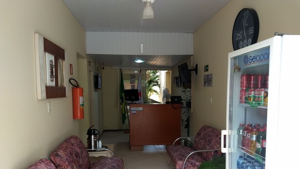A reception area with two patterned chairs, a refrigerator stocked with beverages, and a clock on the wall. - Hotel Pousada do Sol (Uba)