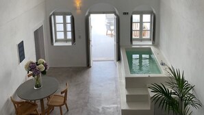 A spacious room with a high arched ceiling, a small pool, a dining area with a table and chairs, and a staircase leading to an upper level. - Imer Villas (Santorini)